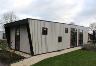 Modern lodge met hoge ramen en verticale panelen bij Just Nature in Kaatsheuvel, Nederland, omgeven door groen.