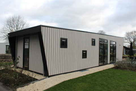 Et moderne lodgehus med store vinduer, omgivet af grønt græs, ved Just Nature i Kaatsheuvel, Holland.