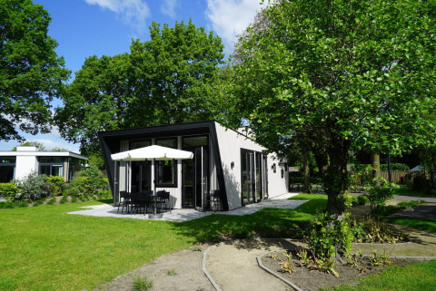 Casa pequeña Just Nature con terraza moderna y sombrilla, rodeada de árboles y césped verde.