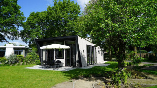 Casa pequeña Just Nature con terraza moderna y sombrilla, rodeada de árboles y césped verde.