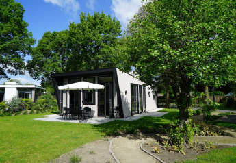 Tiny house Just Nature met eigentijds terras en parasol, omringd door weelderige bomen en gras.