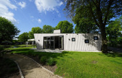 Kleines Haus Just Nature in Kaatsheuvel, Niederlande, von grünem Rasen und Bäumen umgeben.