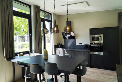 Cuisine noire moderne dans une tiny house avec grandes fenêtres, coin repas et suspensions à Kaatsheuvel, Pays-Bas.
