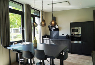 Cocina moderna negra en una tiny house con ventanas grandes, mesa comedor y lámparas colgantes en Kaatsheuvel, Países Bajos.
