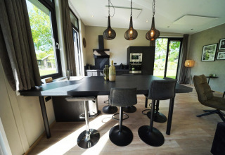 Cucina moderna e zona pranzo in una tiny house a Kaatsheuvel, Paesi Bassi, con grandi finestre e lampade a sospensione.