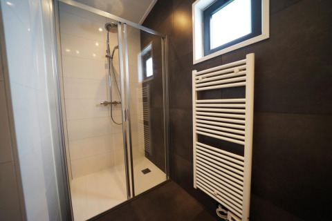 Douche moderne et radiateur sèche-serviettes dans une tiny house à Kaatsheuvel, Pays-Bas, carrelage sombre.