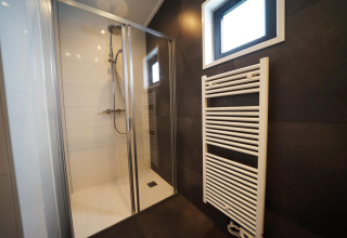 Ducha moderna y radiador toallero en un tiny house de Kaatsheuvel, Países Bajos, con baldosas oscuras.