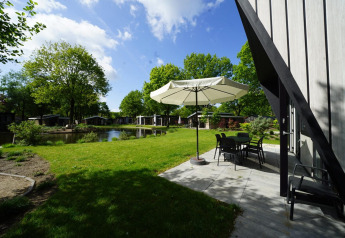 Terras van tiny house Just Nature in Kaatsheuvel, Nederland, met zicht op tuin, vijver en chalets.
