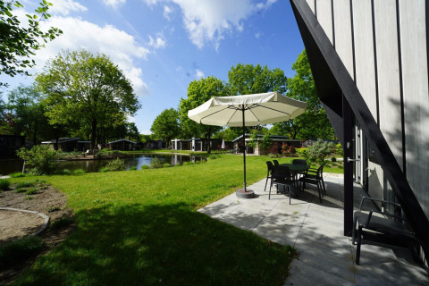 Terras van tiny house Just Nature in Kaatsheuvel, Nederland, met zicht op tuin, vijver en chalets.