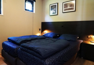 Chambre de la tiny house Just Nature à Kaatsheuvel, Pays-Bas, avec lit bleu et décor moderne, lampes douces.