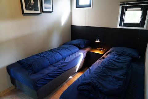 Due letti singoli con biancheria da letto blu scuro in una piccola stanza di Just Nature tiny house a Kaatsheuvel, Paesi Bassi.