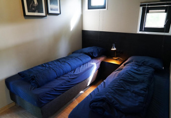Twee enkele bedden met donkerblauw beddengoed in een klein kamertje in Just Nature tiny house in Kaatsheuvel, Nederland.