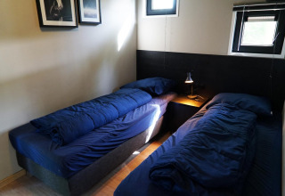 Deux lits simples avec une literie bleu foncé dans une petite chambre chez Just Nature tiny house à Kaatsheuvel, Pays-Bas.