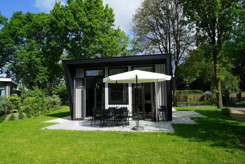 Tiny house moderne Just Nature à Kaatsheuvel, Pays-Bas, entourée d'arbres et de pelouse verdoyante.