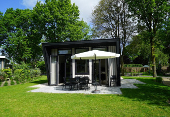 Moderne tiny house Just Nature in Kaatsheuvel, Nederland, omringd door gras en hoge bomen.