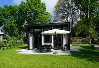 Moderne tiny house Just Nature in Kaatsheuvel, Nederland, omringd door gras en hoge bomen.