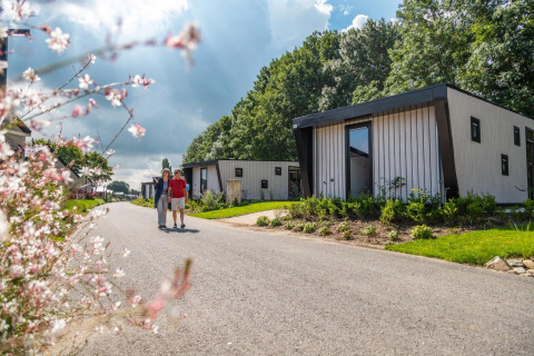 Twee mensen wandelen langs Just Nature tiny house in Kaatsheuvel, Nederland, tussen het groen.