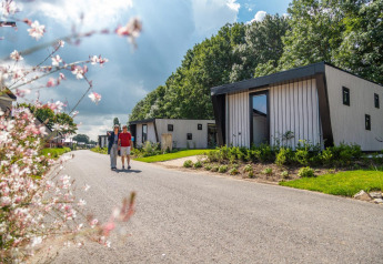 Zwei Menschen spazieren vor dem Just Nature Tiny House in Kaatsheuvel, Niederlande, entlang eines Weges.