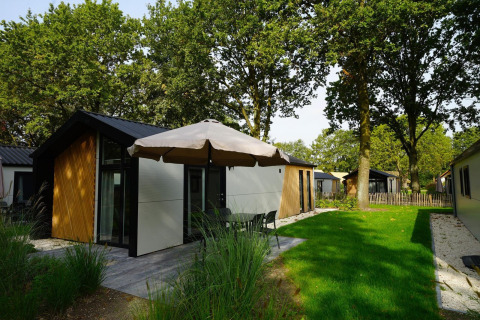Vue extérieure du Kids Adventure cottage avec façade moderne, terrasse, parasol et pelouse verte.