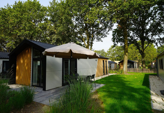 Außenansicht der Kids Adventure cottage mit moderner Fassade, Terrasse, Sonnenschirm und grünem Rasen.