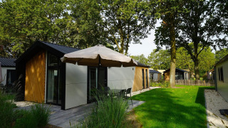 Vista exterior de la Kids Adventure cottage con fachada moderna, terraza, sombrilla y césped verde.