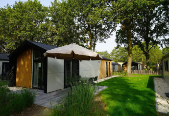 Vista esterna della Kids Adventure cottage con facciata moderna, patio, ombrellone e prato verde.