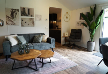 Moderne stue i Kids Adventure cottage, Kaatsheuvel, Holland, med grøn sofa, kunst og stor stueplante.