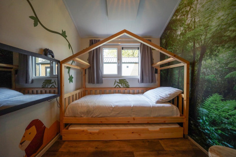 Dormitorio infantil con cama de madera en forma de casa, mural de selva, en Kids Adventure cottage Kaatsheuvel.
