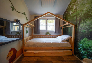 Dormitorio infantil con cama de madera en forma de casa, mural de selva, en Kids Adventure cottage Kaatsheuvel.