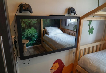 Værelse med køjesenge, spejl-tv, to spilkonsoller og vægmaleri i Kids Adventure cottage i Kaatsheuvel, Holland.