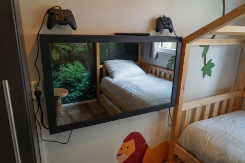 Habitación con literas, TV espejo, dos mandos de consola y decoración selvática en Kids Adventure cottage, Kaatsheuvel, Países Bajos.