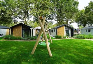 Foto der Kids Adventure Cottage Lodges mit Spielplatz und Schaukel im Grünen in Kaatsheuvel, Niederlande.
