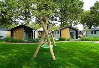 Foto der Kids Adventure Cottage Lodges mit Spielplatz und Schaukel im Grünen in Kaatsheuvel, Niederlande.