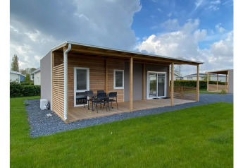 Moderne Cottage 4 lodge ved De Biesbosch i Holland med træterrasse, udemøbler og grøn græsplæne.