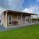 Moderne Cottage 4 lodge ved De Biesbosch i Holland med træterrasse, udemøbler og grøn græsplæne.