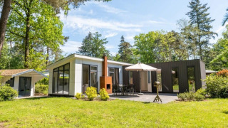Moderna cabaña L-Pavilion 6 en De Biesbosch, Países Bajos, rodeada de árboles verdes y césped soleado.