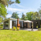 Moderne L-Pavilion 6-lodge i De Biesbosch, Holland, omgivet af grønne træer og solrig græsplæne.