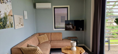 Moderne woonkamer in tiny house Modus 6 bij Marina Strandbad, Nederland, met hoekbank en raam.