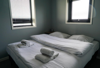 Dormitorio en la tiny house Modus 6 en Marina Strandbad, Países Bajos, con dos camas y toallas blancas.