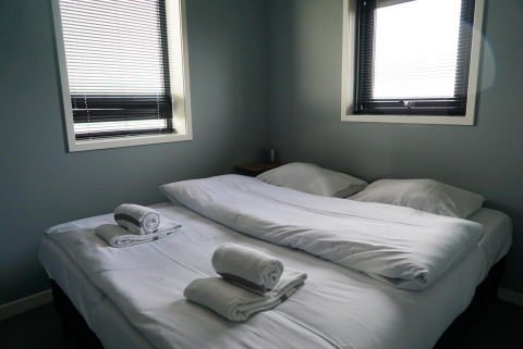 Camera da letto nella tiny house Modus 6 a Marina Strandbad nei Paesi Bassi, con due letti e asciugamani bianchi.