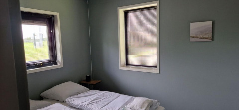 Dormitorio en una tiny house en Marina Strandbad, Países Bajos, con dos ventanas y camas individuales.