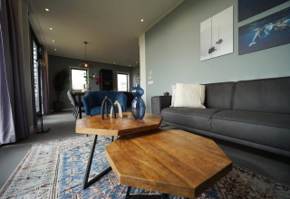 Moderne woonkamer in tiny house Modus 6 bij Marina Strandbad, Nederland, met grijze bank en houten tafels.