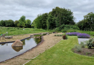 Tuin met vijver, bloemen en houten constructie bij Marina Strandbad, vanaf Modus 6 tiny house in Nederland.