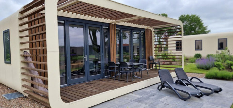 Moderne tiny house Modus 6 bij Marina Strandbad in Nederland met houten terras en ligbedden buiten.