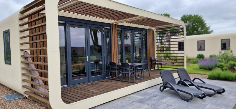 Modern tiny house Modus 6 at Marina Strandbad in the Netherlands with a wooden terrace and lounge chairs.