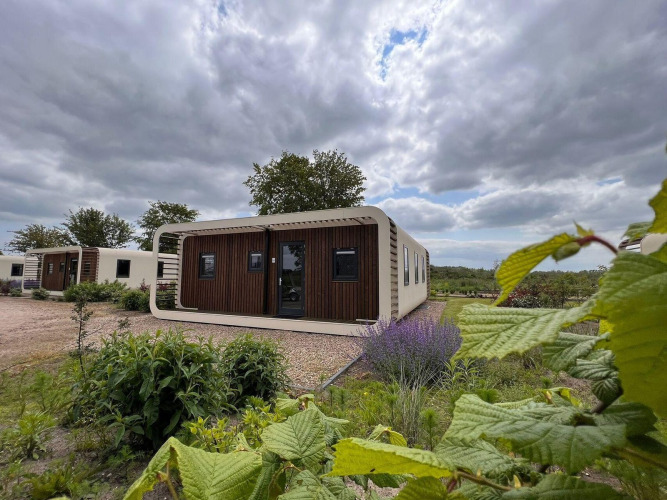 A modern tiny house called Modus 6 at Marina Strandbad in the Netherlands, surrounded by gardens and trees.