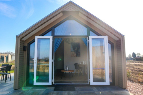 Strandhus 4-lodge med åbne glasdøre, moderne facade og sollys, terrasse og udsigt til naturen.
