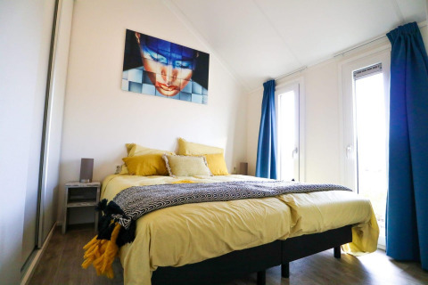 Moderne slaapkamer in Beach House 4 bij Marina Strandbad Nederland, met geel beddengoed en blauwe gordijnen.