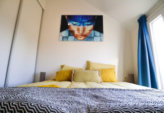 Slaapkamer in Beach House 4 bij Marina Strandbad, Nederland, met moderne kunst boven het bed en blauwe gordijnen.