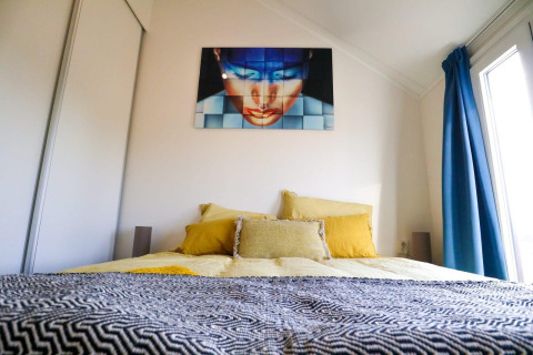 Camera da letto nella Beach House 4 al Marina Strandbad, Paesi Bassi, con arte moderna sopra il letto e tende blu.